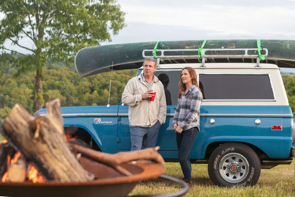 Live your adventure in an Early Bronco with a canoe on top and fire pit in front